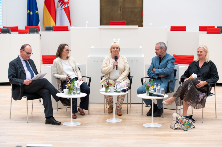 Landtagspräsidentin Prof. Dr. Ulrike Liedtke (m.) begrüßt zur Veranstaltung „Forum Demokratie“ die Podiumsteilnehmer/-innen und Gäste im Plenarsaal des Landtages.