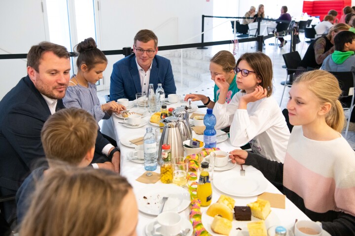 Die Abgeordneten Daniel Keller (l.) und Sebastian Walter (m.)  mit Kindern an der Kuchen- und Kakaotafel im gemeinsamen Gespräch.