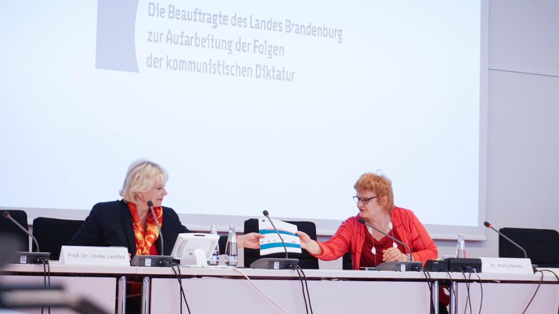 Landtagspräsidentin Prof. Dr. Ulrike Liedtke (l.) nimmt den 5. Tätigkeitsbericht von der Beauftragte des Landes Brandenburg zur Aufarbeitung der Folgen der kommunistischen Diktatur (LAkD) Dr. Maria Nooke (r.) entgegen.