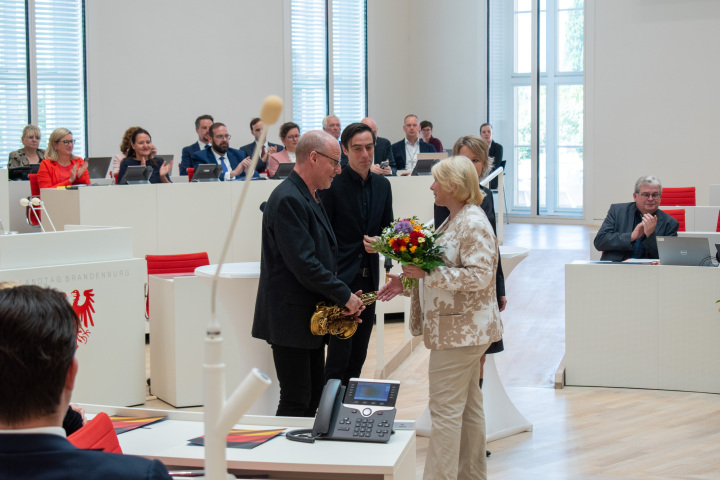 Landtagspräsidentin Prof. Dr. Ulrike Liedtke (r.) bedankt sich bei dem Saxophonisten Ralf Benschu (l.).